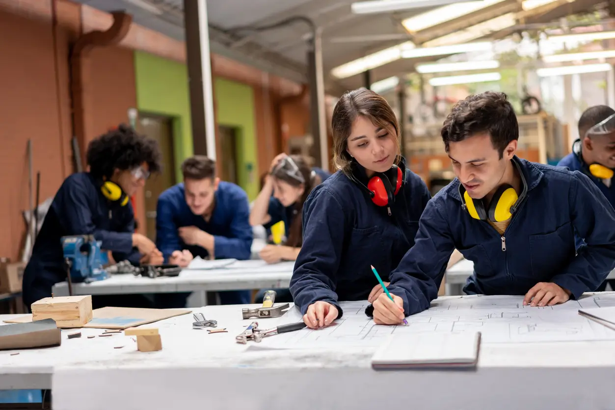 Schülerinnen und Schüler in Overalls an Privatschulen im Kanton Solothurn arbeiten gemeinsam an technischen Zeichnungen.