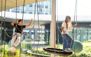 Zwei Kinder balancieren auf Spielplatzschaukeln in einer modernen Aussenanlage der Privatschule Zürich.