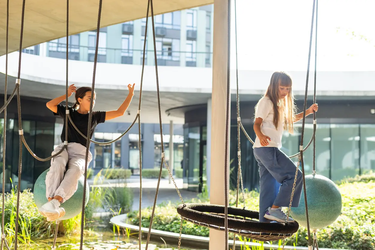 Zwei Kinder balancieren auf Spielplatzschaukeln in einer modernen Aussenanlage der Privatschule Zürich.