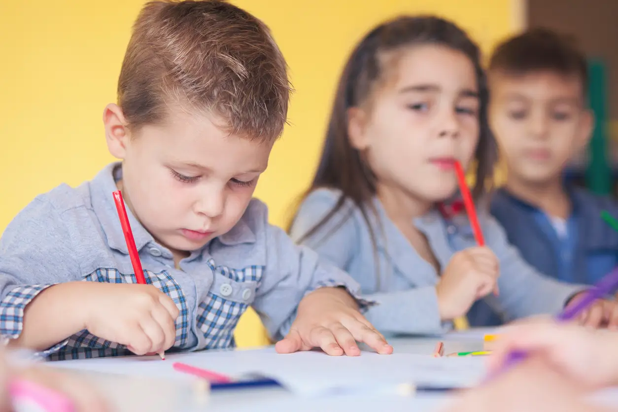 Drei kleine Kinder sitzen an einem Tisch und zeichnen und denken mit Buntstiften.