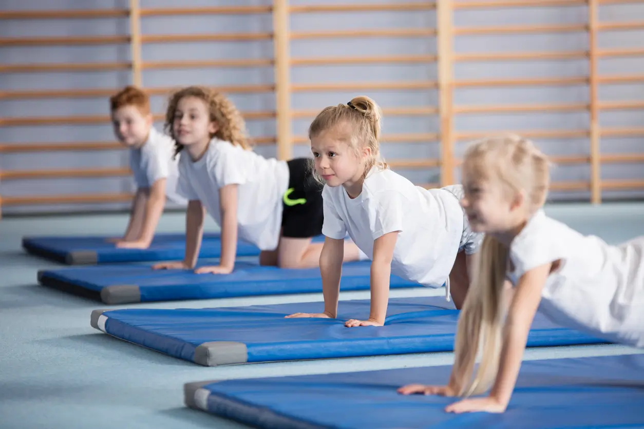 Kinder einer Privatschule im Kanton Solothurn beim Yoga auf blauen Matten in einer Turnhalle.
